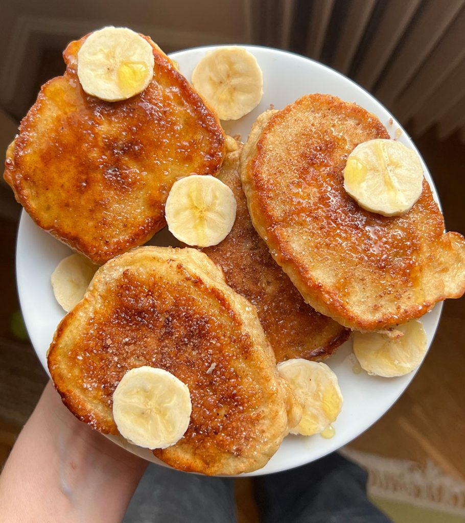 En hand håller fram en vit tallrik med "krabbelurer" och bananskivor. 